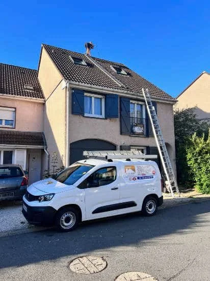 Artisan couvreur sur le toit d'un pavillon, véhicule d'intervention devant la maison